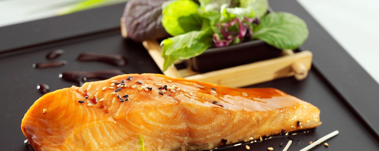 Lachsfilet garniert mit Sauce und Gemüse auf einem dunklen Teller